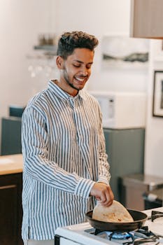 A young man joyfully cooking flatbread on a stove in a stylish and modern kitchen setting.