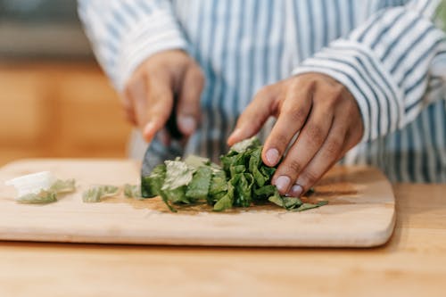 Crop man cutting green leaves while preparing healthy food in kitchen