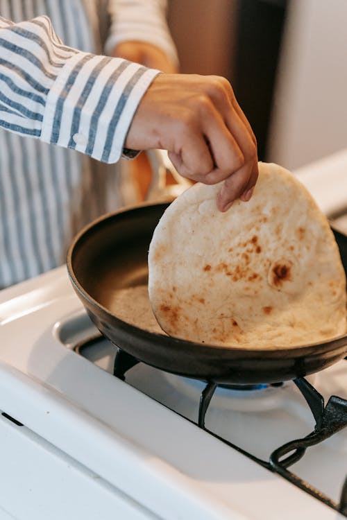 Free Crop anonymous male cook preparing traditional Indian chapati bread in pan placed on stove in kitchen at home Stock Photo