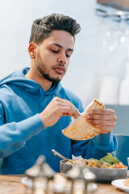 Focused ethnic male tasting delicious aromatic white bread at table with dish filled with meal