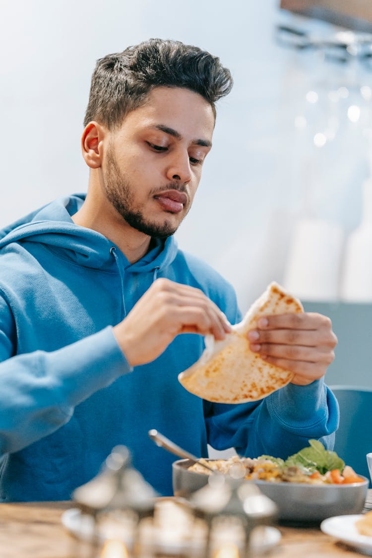 Indian Man Eating White Bread At Table With Food