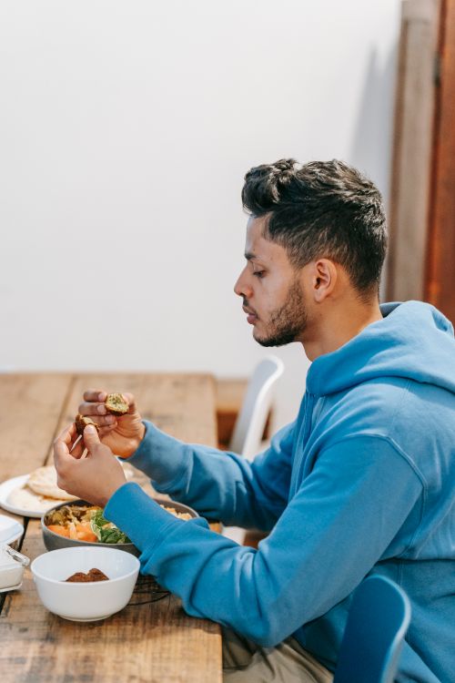 Free Side view of crop ethnic male in blue hoodie eating tasty dinner at timber table Stock Photo