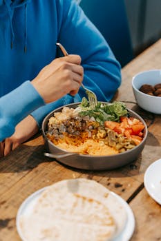 From above of crop unrecognizable male having meal with fork at table with food in plates
