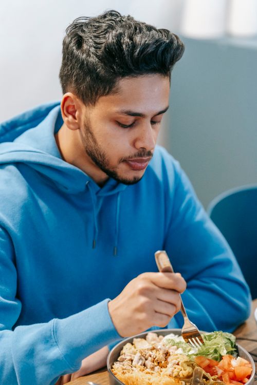 Free Bearded young ethnic male in blue hoodie tasting fresh delicious food in plate on blurred background Stock Photo