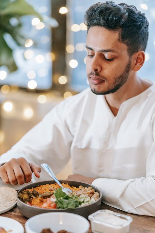 Free A man in traditional attire enjoys a healthy iftar meal with vegetables and pita indoors. Stock Photo