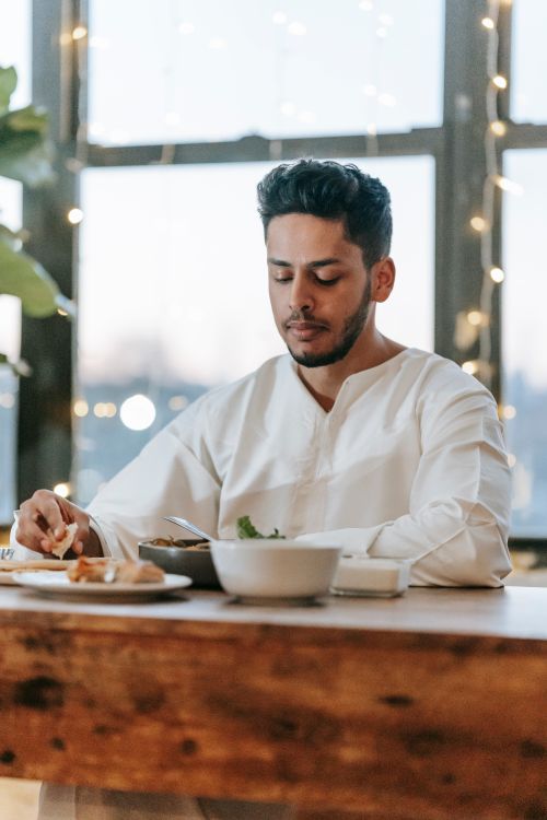 Free A man in traditional attire savoring a meal inside, with string lights creating a cozy ambiance. Stock Photo