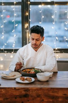 A man enjoys a traditional meal indoors surrounded by string lights, creating a warm ambiance.