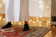 Feet wearing socks on traditional rug with white attire, indoors and festive lighting.