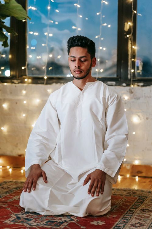 Free Man kneeling in prayer wearing traditional white clothing in a softly lit room. Stock Photo