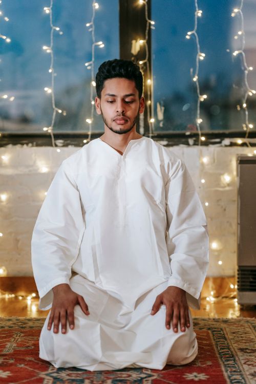 Free A Muslim man kneeling in prayer indoors, surrounded by string lights, depicting peace and devotion. Stock Photo