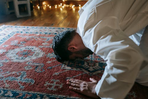 Man in White Thobe Bowing Down on Red and Blue Rug