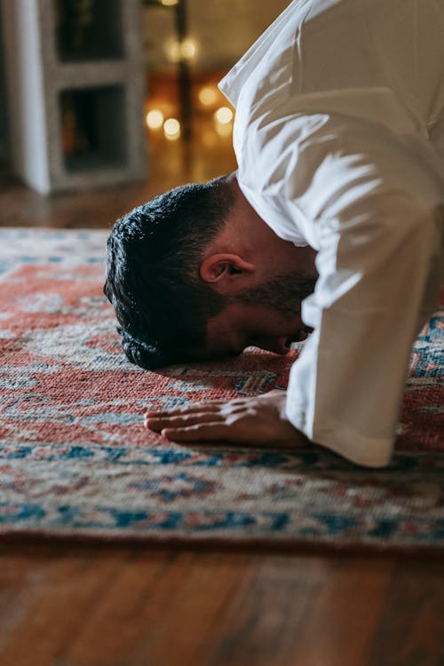 Man in White Thobe Bowing Down on Red and Blue Rug