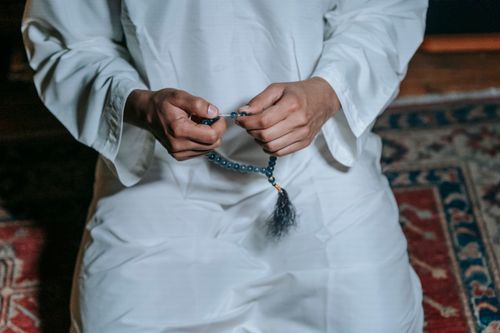 Free Adult in traditional attire holding prayer beads, symbolizing Islamic rituals and spirituality indoors. Stock Photo