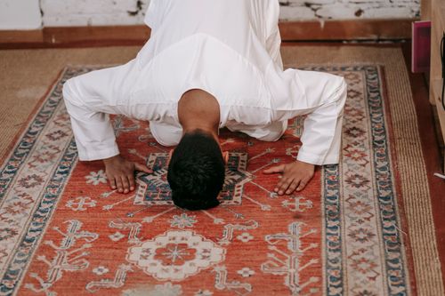 Free A Muslim man in traditional clothing performs salah on a beautifully designed prayer rug inside a room. Stock Photo