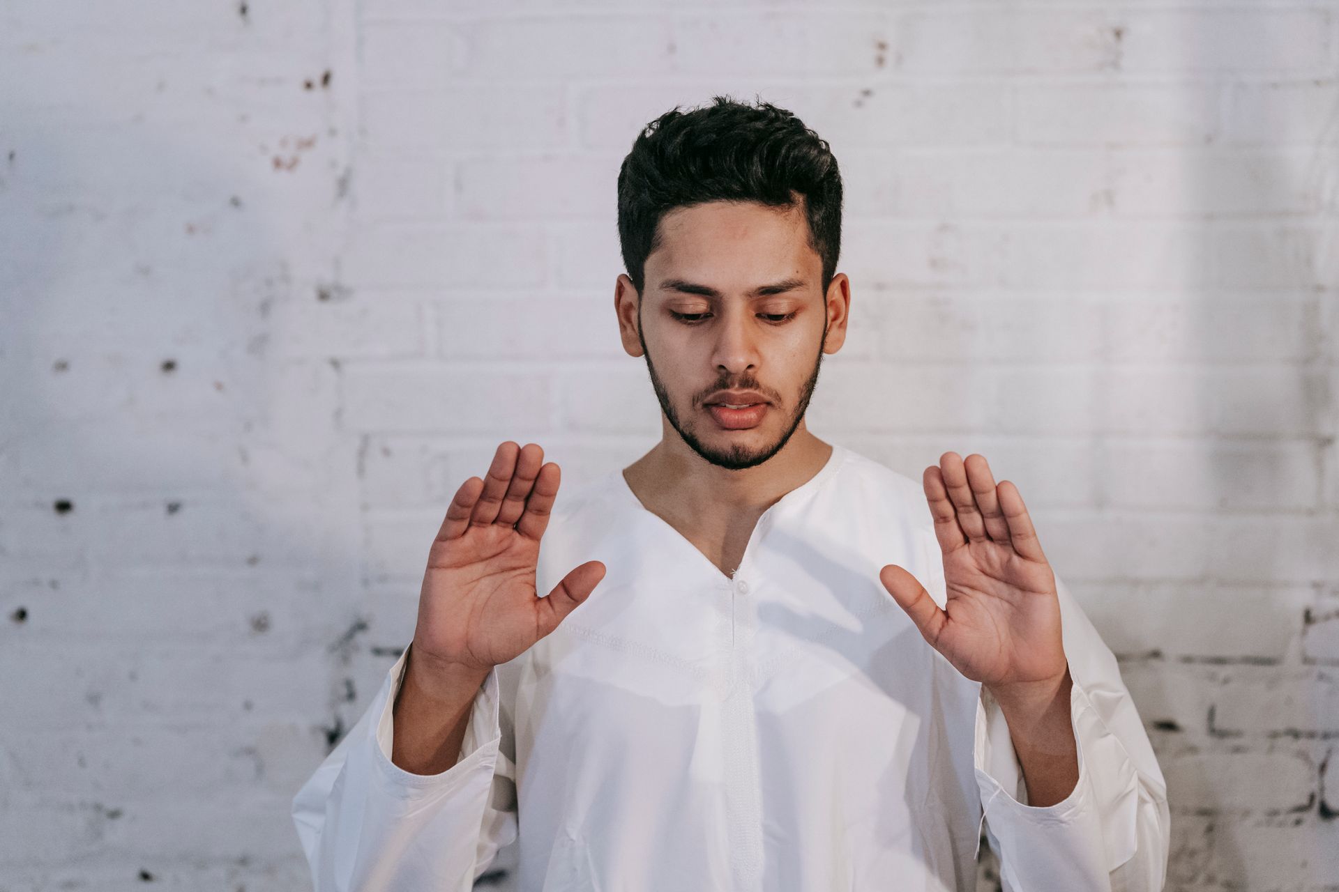 A man in traditional Islamic wear performing a prayer indoors with focus.