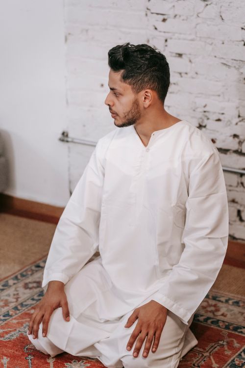 Free A man wearing a white thobe is kneeling in prayer indoors, highlighting Islamic faith and tradition. Stock Photo