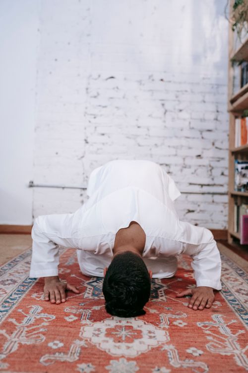 Free A man in traditional attire engaged in prayer, bowing indoors on a patterned rug. Stock Photo