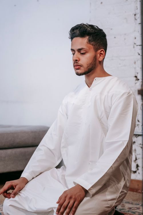 Free A man kneeling and praying indoors in traditional Islamic attire, focused on worship. Stock Photo