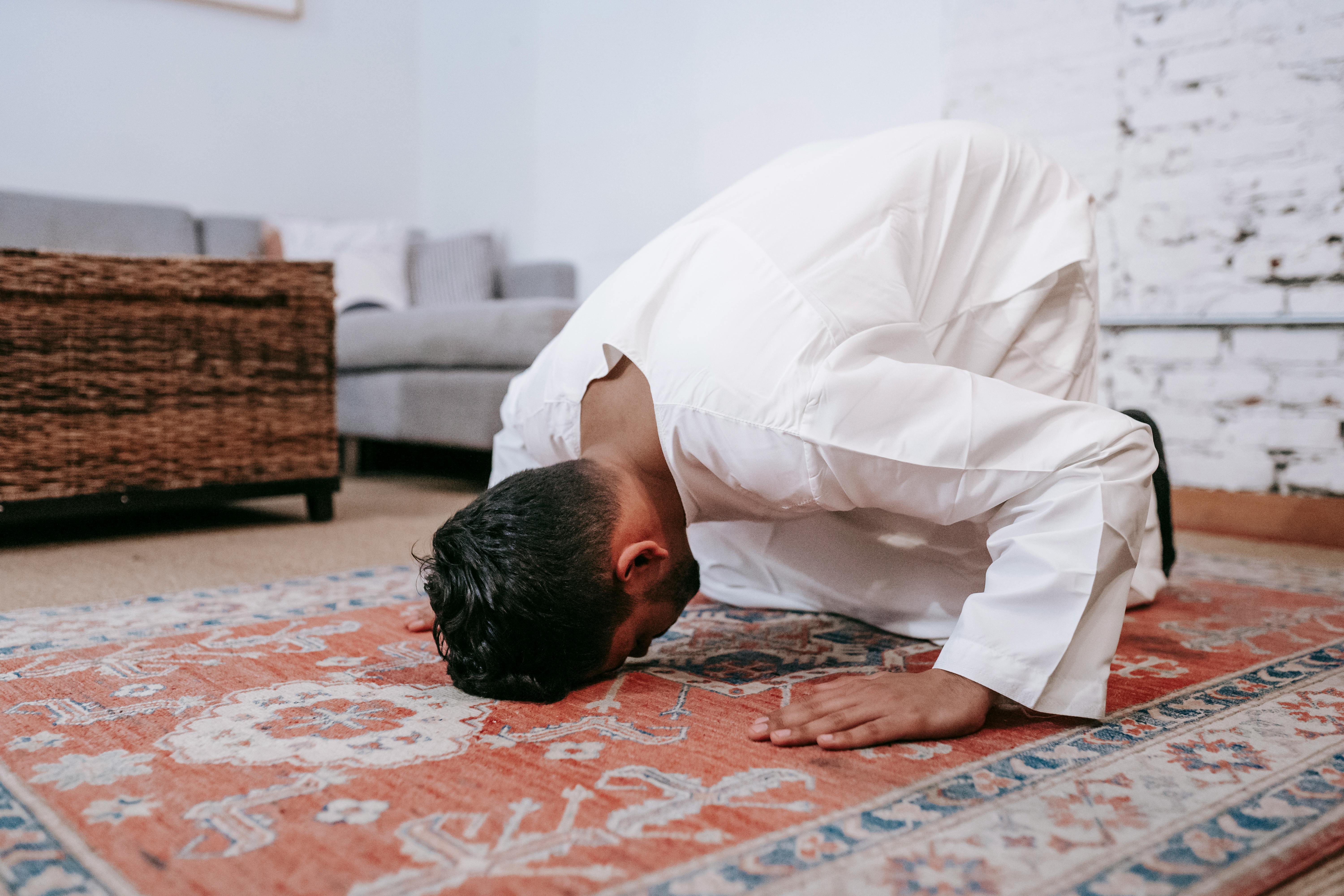 man in white thobe bowing down on red and blue rug