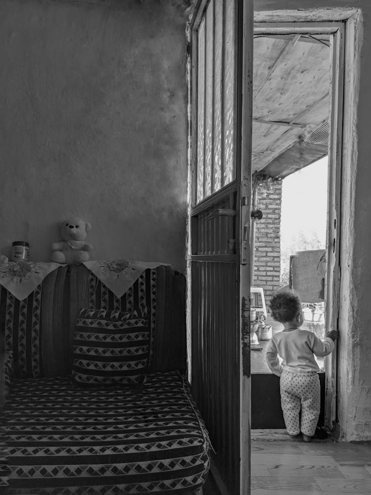 Little Boy Looking Out Of The Balcony Door In An Apartment 