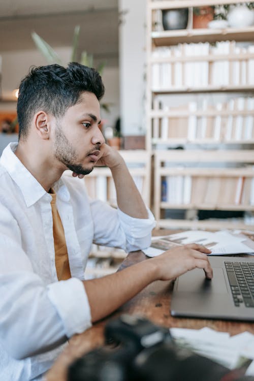 Concentrated ethnic male sitting at table and working on laptop