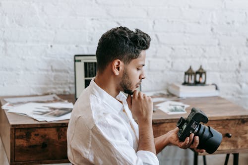 Serious ethnic man with photo camera near table with netbook