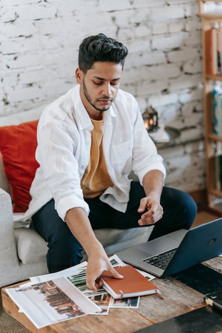A young Hispanic male designer is seen taking a planner from a table adorned with a laptop and various project images, embodying the essence of creativity and organization essential for navigating the PaaS talent pool.. Michael Burrows, the eye behind the image