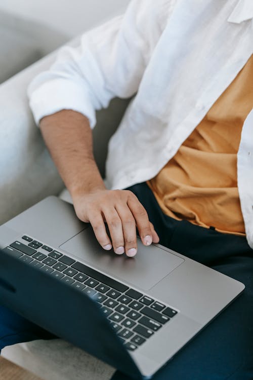 High angle of crop unrecognizable male using touchpad on laptop while surfing internet and working on freelance project at home