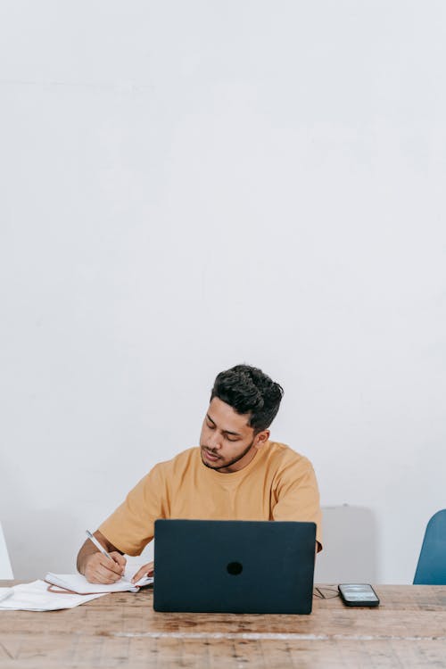Free Remote worker with laptop taking notes Stock Photo