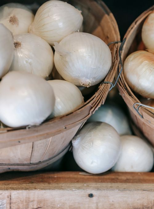 Free High angle of pile of fresh organic white onions in wooden baskets placed on stall in local grocery market Stock Photo