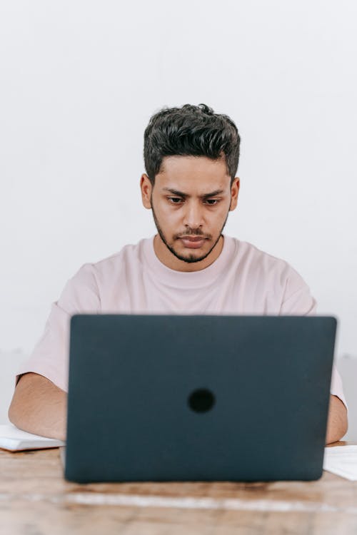 Focused young bearded Hispanic male blogger using laptop while creating content for new blog in social network at workplace