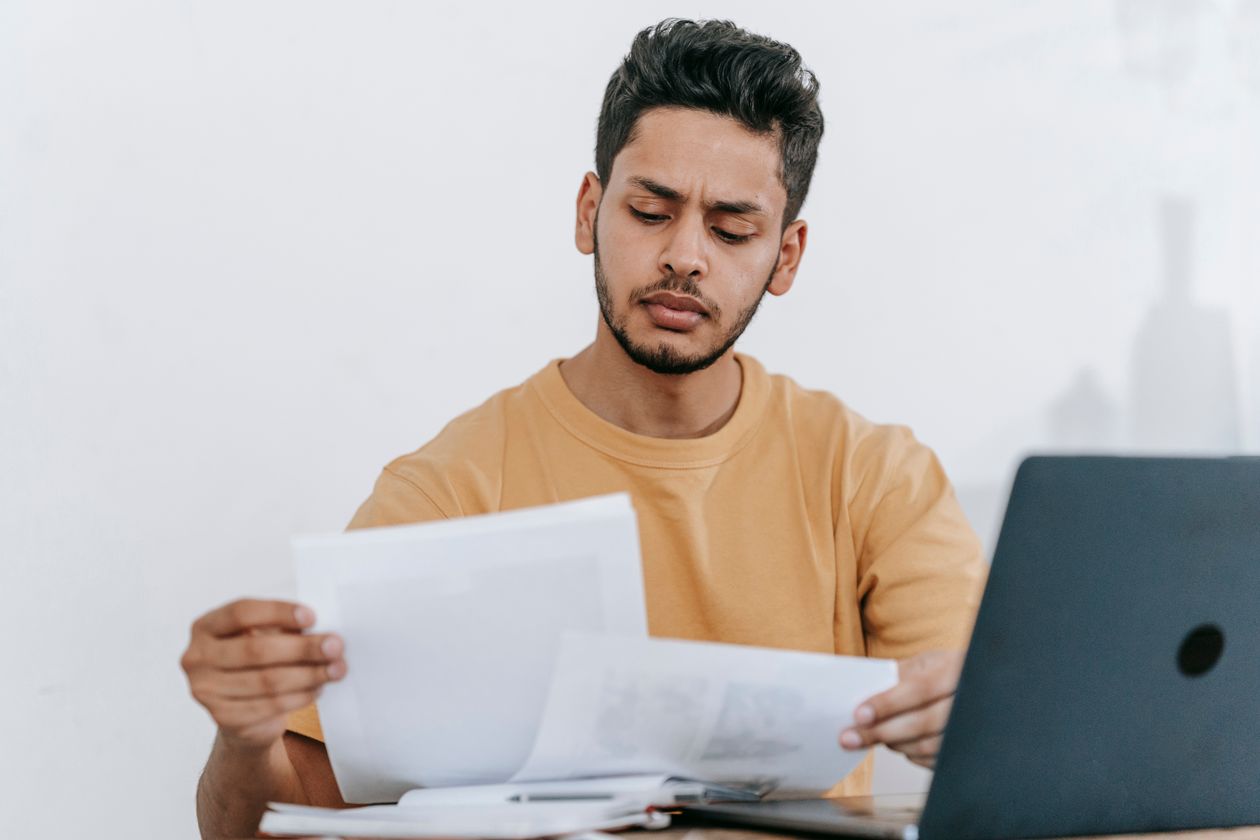 Un homme examine des courriers et des documents posés devant son ordinateur portable