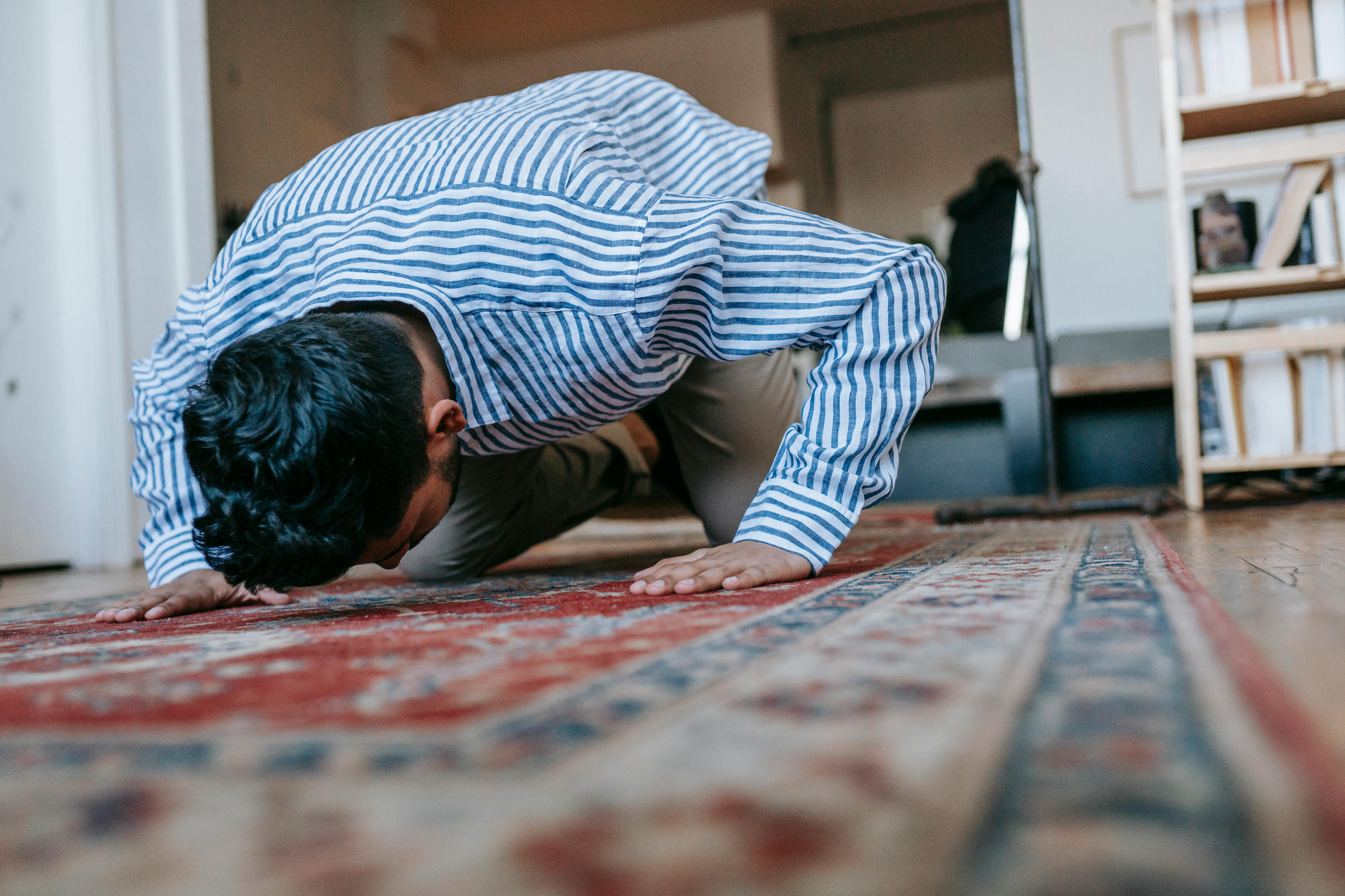 man in blue and white stripe dress shirt bowing down on red and blue area rug