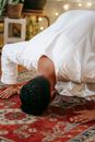 Man in White Thobe Bowing Down on Red and Blue Rug