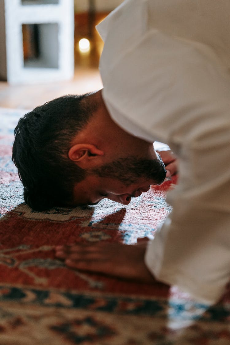 Man In White Thobe Bowing Down On Red And Blue Rug