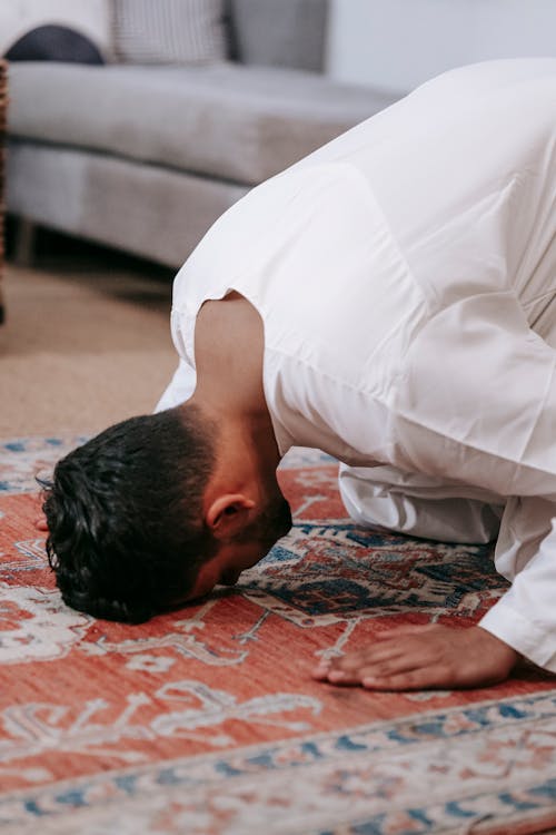 Free Man in White Thobe Bowing Down on Red and Blue Rug Stock Photo