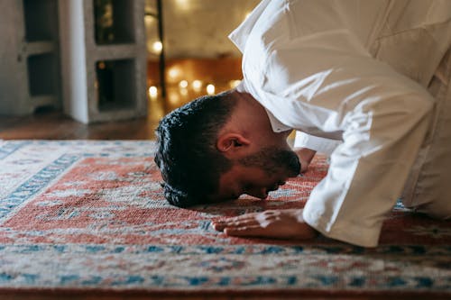 Man in White Thobe Bowing Down on Red and Blue Rug