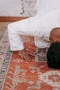 Man in White Thobe Bowing Down on Red and Blue Rug