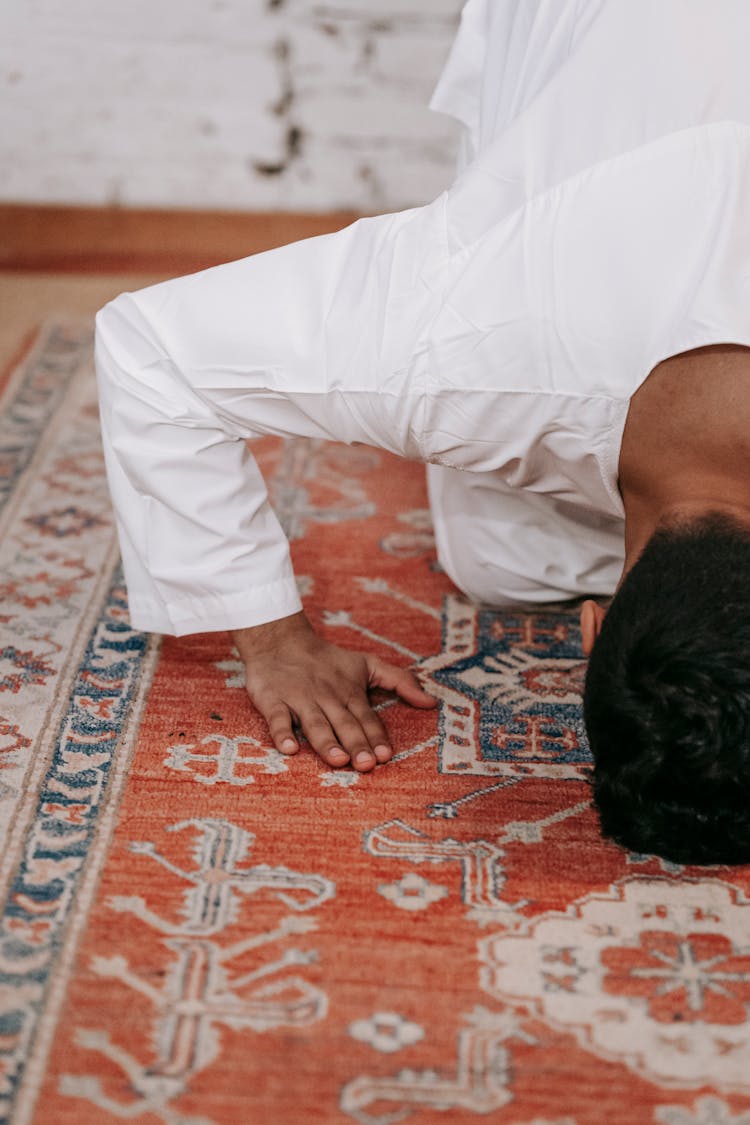 Man In White Thobe Bowing Down On Red And Blue Rug