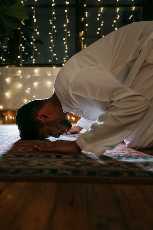 Man in White Thobe Bowing Down on Red and Blue Rug