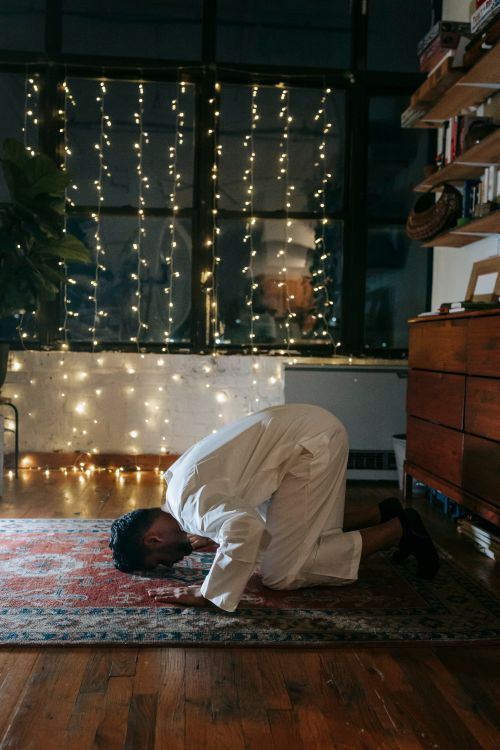 Free A Muslim man kneels in prayer in a warmly lit room adorned with string lights. Stock Photo