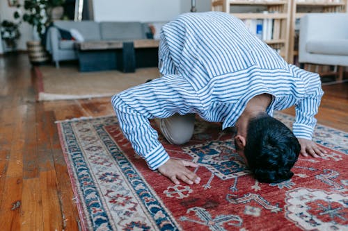 Free Man in Blue and White Stripe Dress Shirt Bowing Down on Red and Blue Area Rug Stock Photo