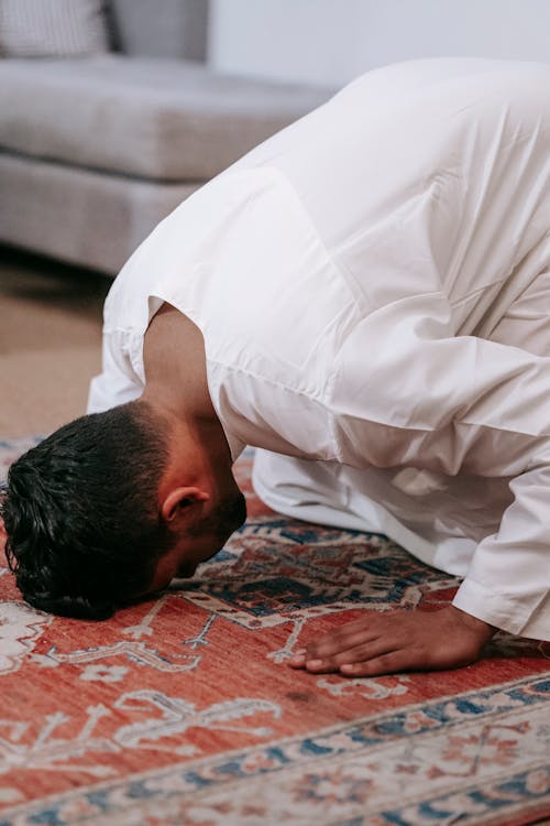 Man in White Thobe Bowing Down on Red and Blue Rug