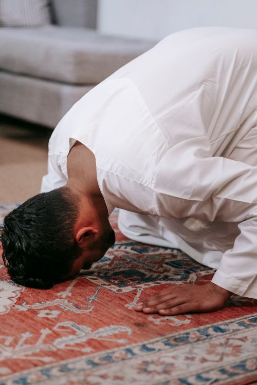 Free A man in traditional attire kneeling in prayer on a rug in a homely setting. Stock Photo