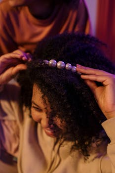 A woman carefully styles her curly hair with a pearl headband, showcasing beauty and elegance.