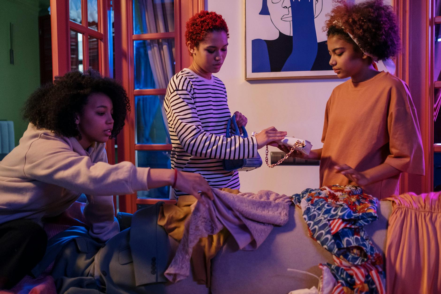 Three women in cozy setting swapping clothes and accessories indoors.