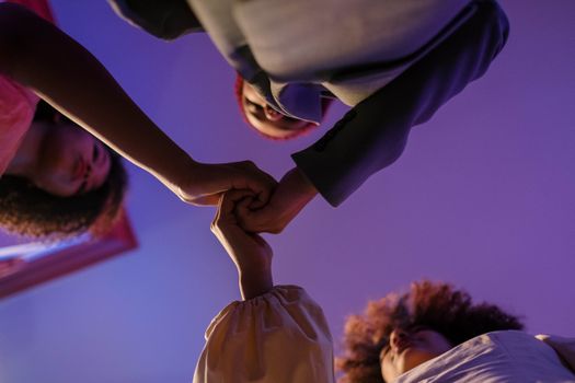 A captivating low-angle view of diverse individuals holding hands against a vibrant purple backdrop.