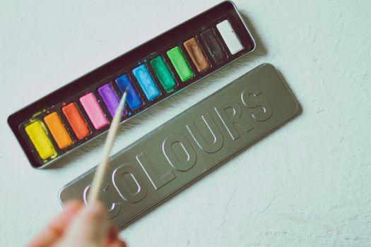 A close-up of a colorful watercolor paint set and brush on a light surface.