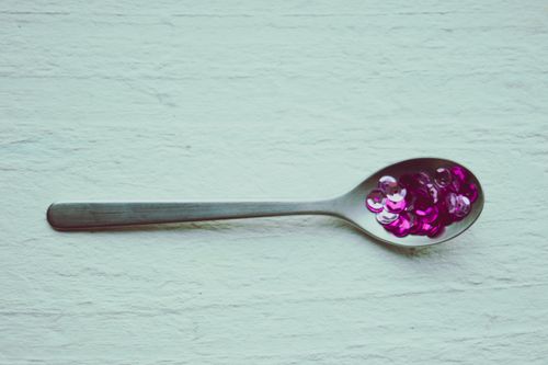Free Close-up of a metal spoon holding vibrant purple sequins against a textured white background. Stock Photo