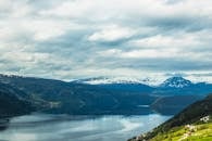 挪威白雪皑皑的山脉与倒映着多云天空的宁静湖泊，令人惊叹